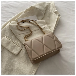 Detail of beige quilted shoulder bag with gold chain strap on a white blazer