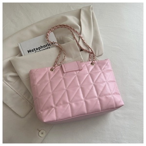 Macro detail of pink quilted tote bag with gold chain strap on stylish blazer