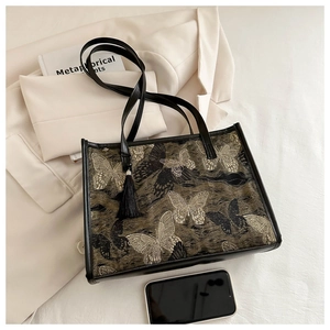 Détail d'un grand sac cabas marron avec broderie papillon et pompons en cuir noir
