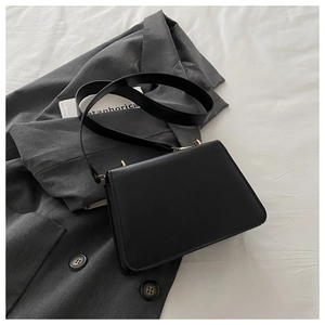 Close-up of black square crossbody bag with gold buckle on grey blazer