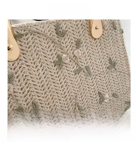 Close-up of straw woven bag featuring green leaf and pink flower embroidery details