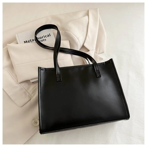 Détail d'un sac cabas noir en cuir PU posé sur un blazer beige au style bureau minimaliste