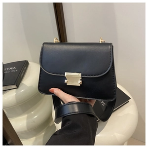 Detail of black crossbody bag featuring gold hardware clasp and wide leather strap