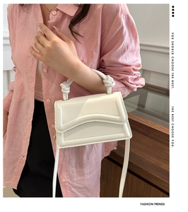 Detail of white square crossbody bag with knot handle and wavy quilted pattern design