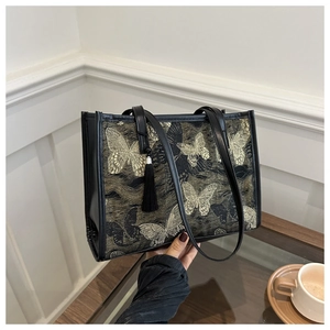 Détail du motif papillon brodé sur sac cabas noir avec bandoulière et pompon en soie