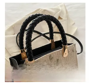 Detail of woven straw handbag featuring green leaf embroidery and black leather handles