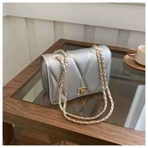 Detail of silver quilted chain bag with gold metal twist lock on a wooden coffee table