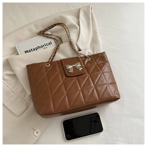 Detailed macro view of brown quilted tote with silver bow buckle on blazer background