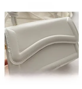 Close-up of white crossbody bag showing refined stitching on the curved flap detail