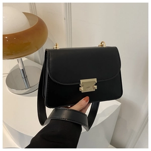 Detail view of a black leather crossbody bag with a gold geometric lock and wide strap