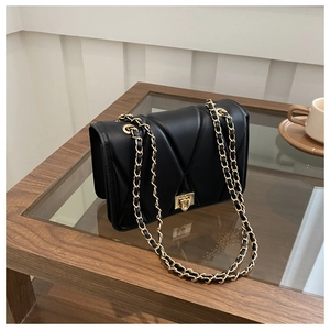 Close-up of black quilted chain bag with gold metal twist lock on a wooden table