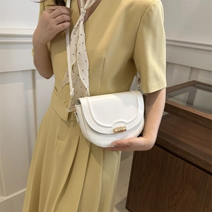 Minimalist white saddle bag with wavy stitching, gold buckle, and polka dot scarf detail