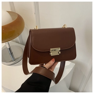 Close-up of deep brown leather crossbody bag with minimalist golden geometric clasp