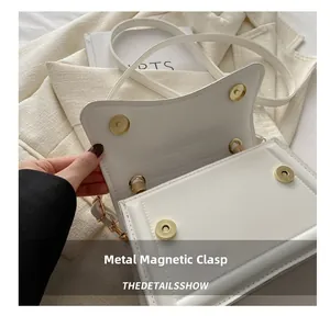 Detail of a white square handbag featuring a golden circular magnetic snap closure hardware