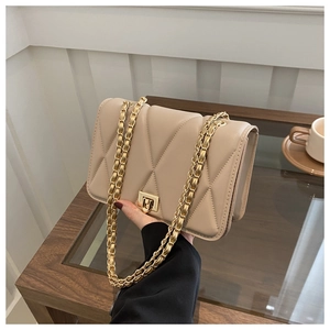 Detail of beige quilted chain bag with gold metal clasp shown on a person