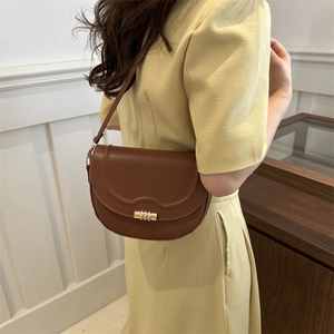 Brown semi-circular saddle bag with gold cylinder lock worn by a model in yellow dress