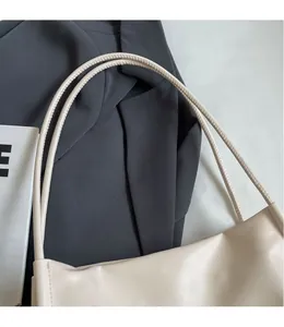 Dettaglio dei doppi spallacci sottili di una borsa sottobraccio minimalista color panna