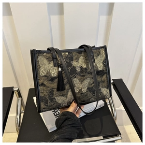 Détail d'un sac cabas en tissu noir avec broderie papillon dorée élégante et gland décoratif