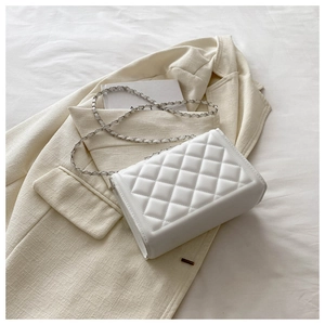 Close-up of white quilted crossbody bag with chain strap on an off-white blazer