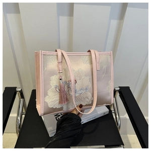 Détail de broderie sur un sac cabas en satin rose avec motifs floraux et pompon décoratif