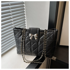 Detail of black quilted tote bag with silver bow fastener and chain straps