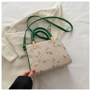 Detail of beige straw handbag featuring delicate floral embroidery and green woven handles