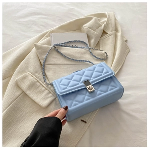 Detail of light blue quilted chain crossbody bag on white blazer with silver clasp