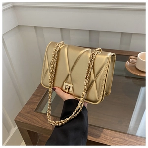 Detail of gold quilted crossbody bag with metal chain strap and twist lock closure