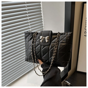 Detailed shot of black quilted tote bag featuring silver bow buckle and chain strap