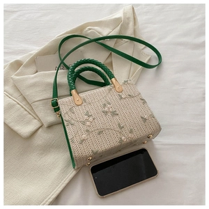 Detail of straw woven bag with floral embroidery and green braided handles