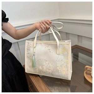 Détail du sac cabas crème avec imprimés floraux classiques et pompon décoratif vert