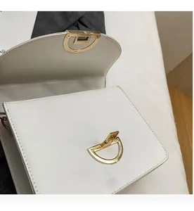 Detail of white leather handbag featuring gold D-shaped twist lock hardware on a textured surface