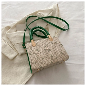 Detail of straw woven bag with green floral embroidery and adjustable leather shoulder strap