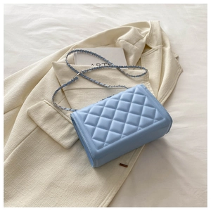Detail of light blue quilted chain bag on beige blazer background with prop accessories