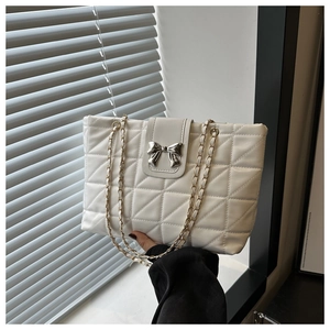 Detail of white quilted tote bag featuring silver bow clasp and chain strap