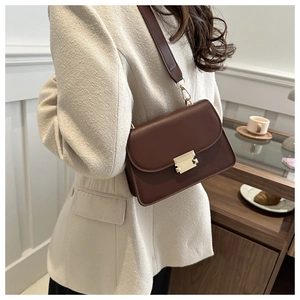 Detail of dark brown leather crossbody bag featuring gold hardware and wide shoulder strap