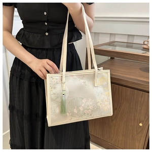 Détail de broderie florale et pompon vert sur un sac cabas beige élégant
