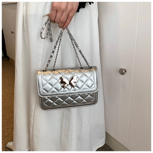 Détail du sac argenté matelassé avec fermoir papillon métallique et bandoulière chaîne
