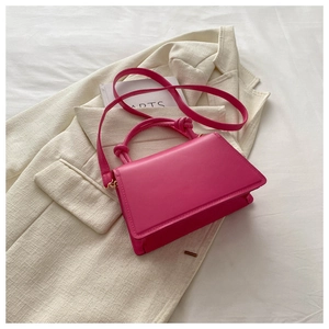Detail of magenta leather handbag with knotted handles on an off-white blazer
