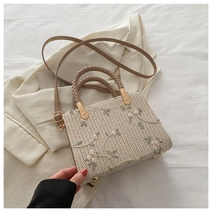 Detailed close-up of straw woven bag with floral embroidery and gold metal bottom studs