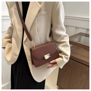 Detail of a brown leather crossbody bag featuring a golden rectangular clasp and wide strap