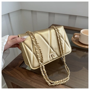 Elegant champagne gold quilted chain shoulder bag with metal lock on a glass table