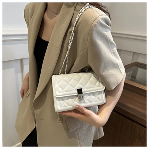 Detail view of a white quilted leather bag with silver lock and chain strap on a model