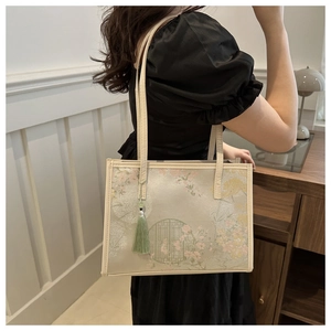 Detail of floral embroidery on a white tote bag with green tassel and long shoulder straps