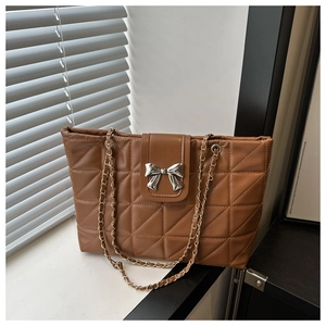Close-up of caramel brown quilted tote bag featuring a silver metal bow and chain strap