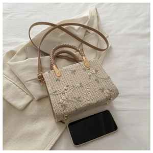 Detail of straw woven handbag featuring floral embroidery and adjustable strap for women