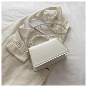 Detail of white minimalist handbag with knotted handle and shoulder strap on blazer