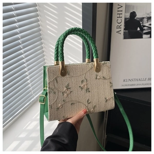 Detail of straw woven bag with green floral embroidery and adjustable leather strap