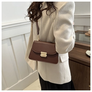Detail of a dark brown leather flap bag with a golden metal buckle worn by a model