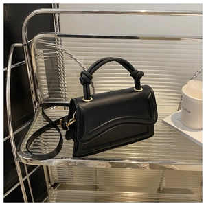 Detail of black handbag featuring a knotted handle and unique wavy-edge flap with gold buckle